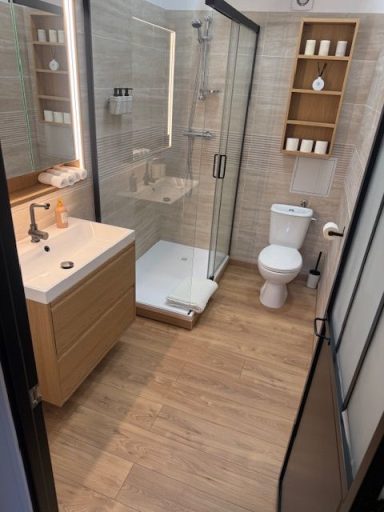 Salle de bain moderne avec douche, lavabo, toilettes et étagère en bois.
