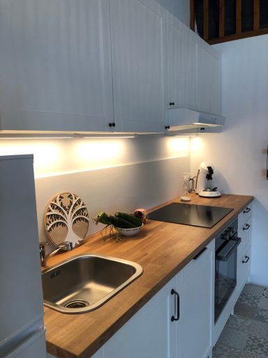 Cuisine moderne avec plan de travail en bois, évier, plaques de cuisson et éclairage.