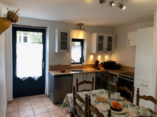 Cuisine lumineuse avec une table, des chaises et des armoires blanches. Ambiance accueillante.