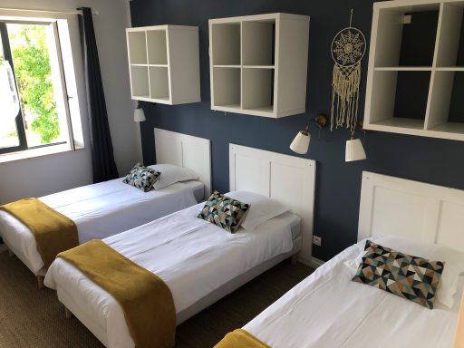 Chambre avec trois lits simples, murs bleu foncé et décor moderne.