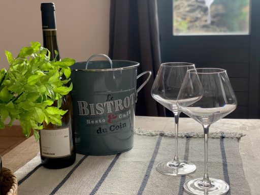 Bouteille de vin, seau, deux verres à vin et plante à côté d'une fenêtre.