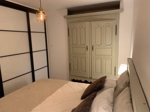 Chambre sommaire avec lit, coussins et armoire aux portes vertes.
