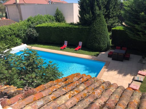 Piscine bleue entourée de verdure et chaises longues rouges dans un jardin.