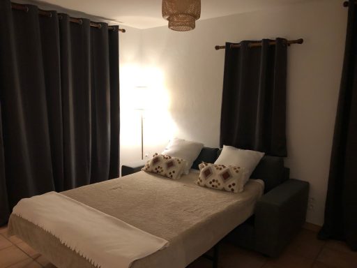 Chambre avec lit, coussins décoratifs et rideaux foncés, éclairage agréable.