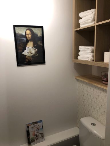 WC décoratifs avec cadre Mona Lisa – Gîte Carpe Diem Toilettes avec une affiche de Mona Lisa et des serviettes empilées sur une étagère.