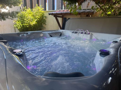 Baignoire à remous remplie d'eau, avec des lumières LED, entourée de verdure.